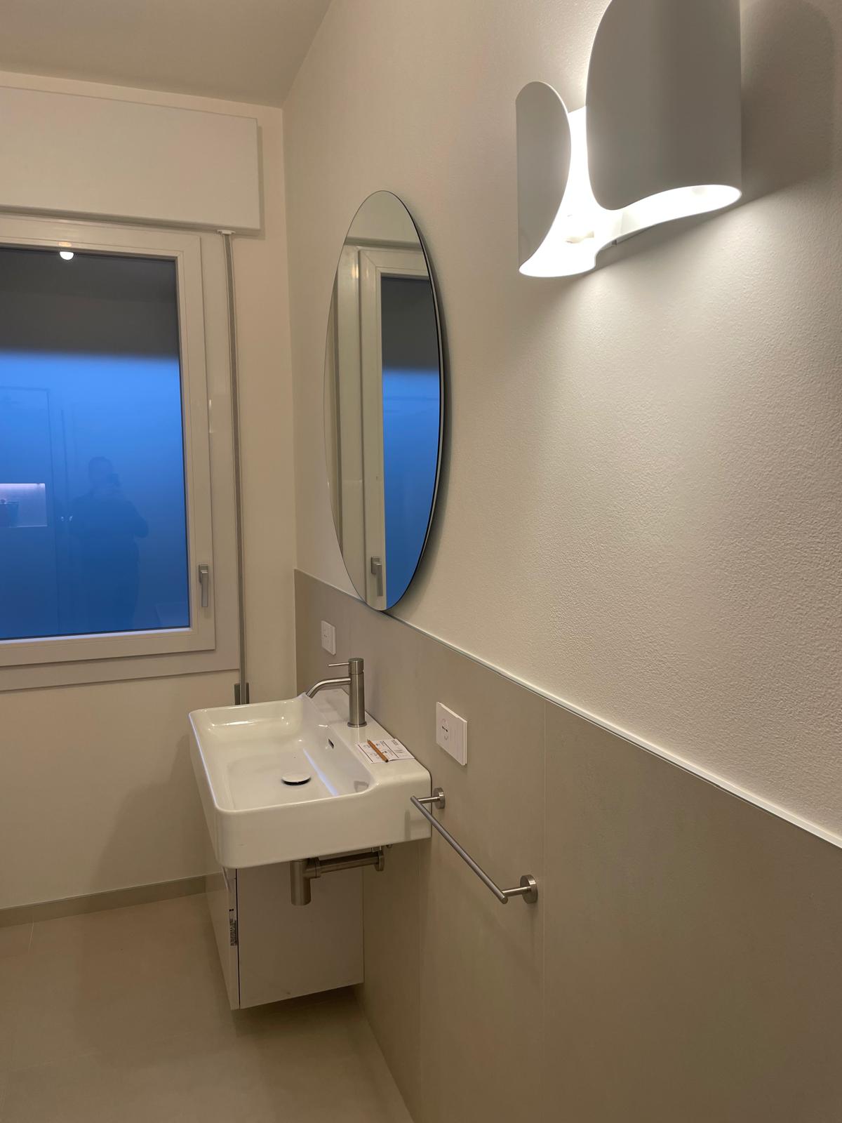 Bagno moderno chiavi in mano a Padova con lavabo sospeso, specchio ovale e illuminazione a parete
